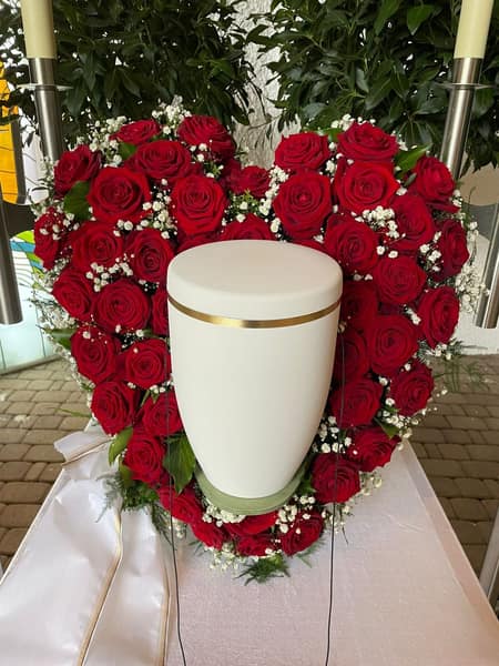 Herz aus roten Rosen, davor eine helle Urne