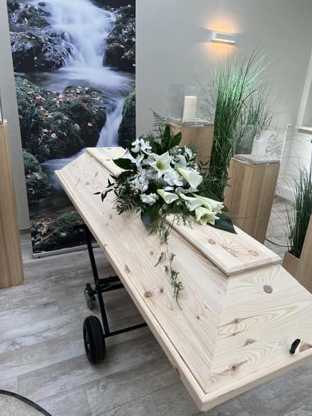Heller Sarg mit weißem Blumenschmuck im Abschiedsraum