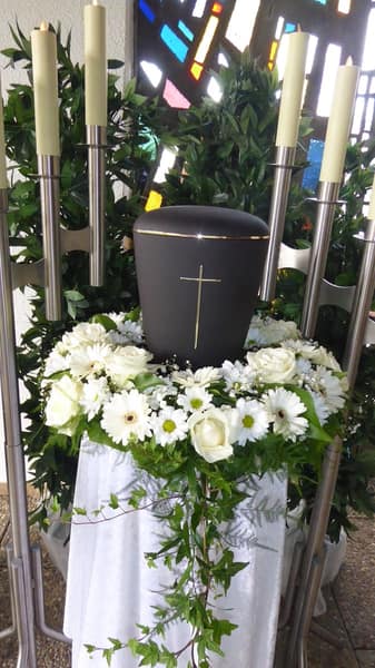 Urne mit weißem Blumenschmuck zwischen hohen Kerzen