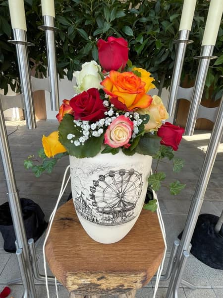 Urne mit Rosenschmuck zwischen Kerzen