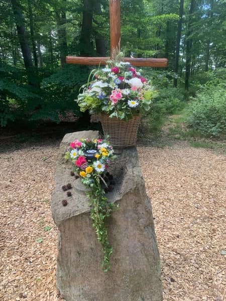 Urne mit Blumenschmuck auf einem Stein im Wald